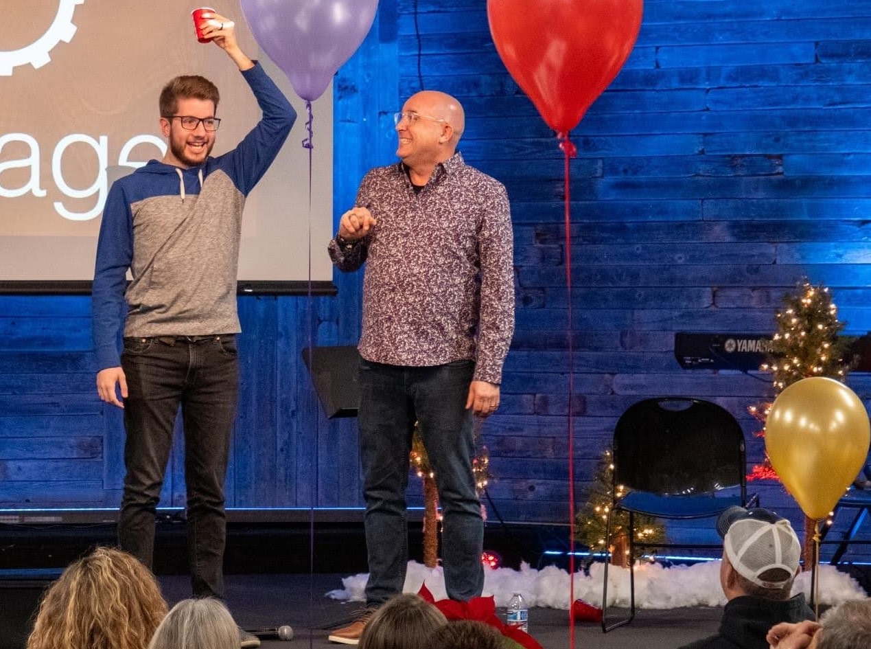 Tim and a volunteer on stage with red cups and balloons