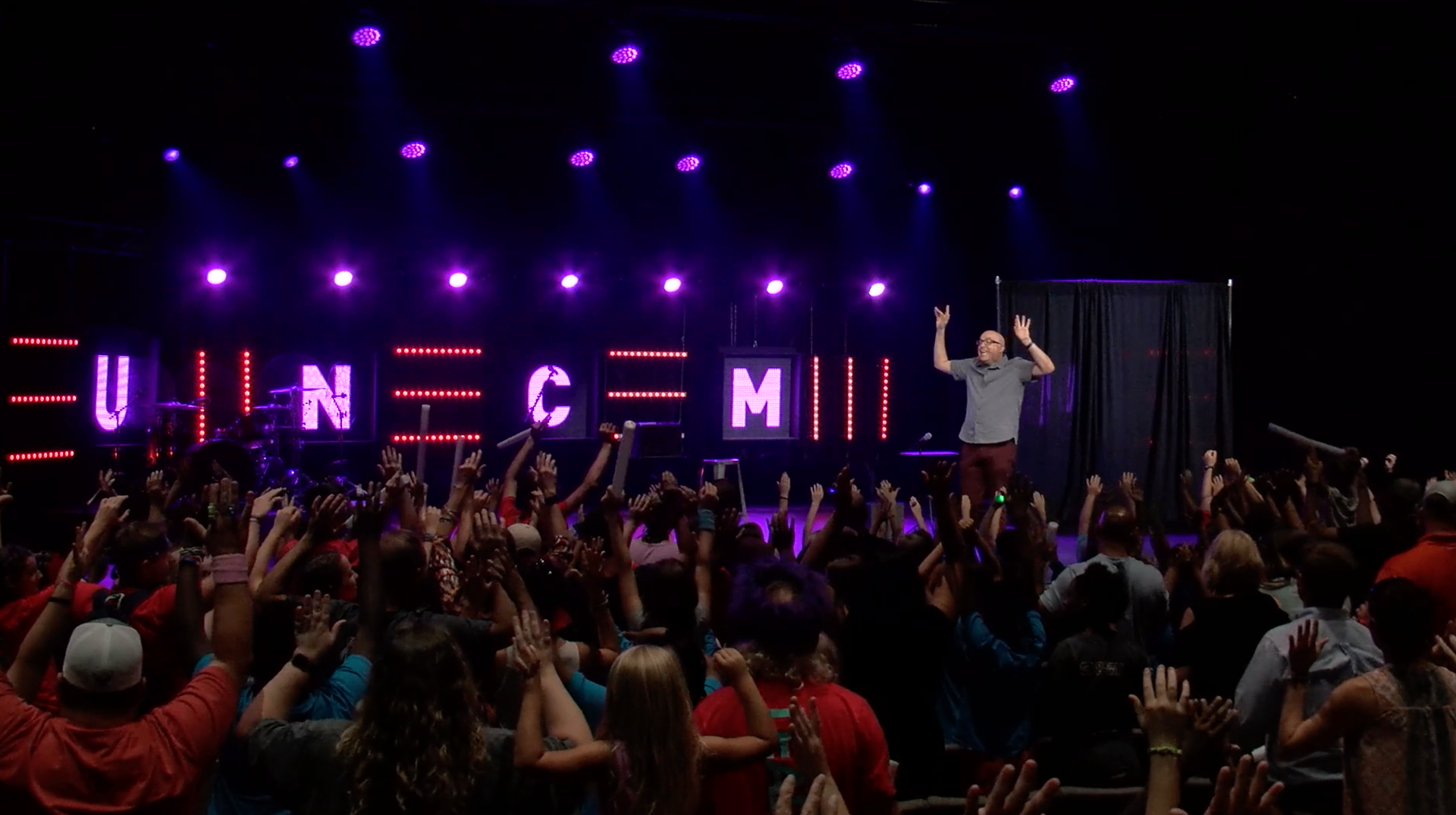 Wide crowd shot with hands raised toward Tim on stage
