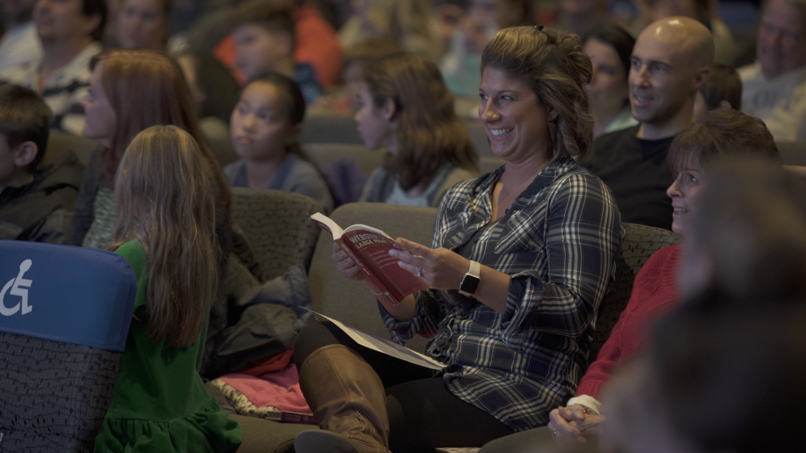 A woman in the audience laughing while reading from a book during a mentalism routine